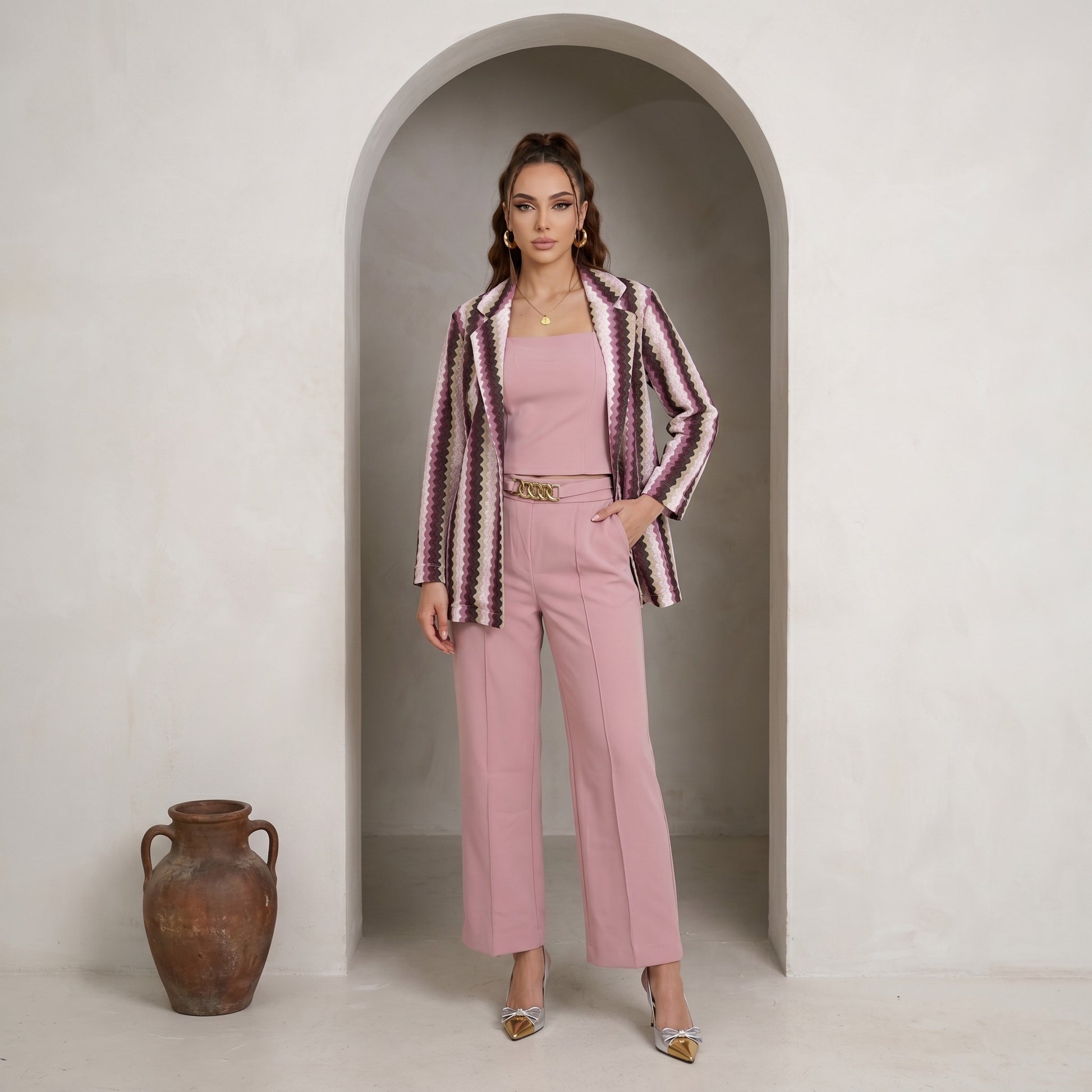 Woman in a pink outfit with a patterned jacket standing in an archway.